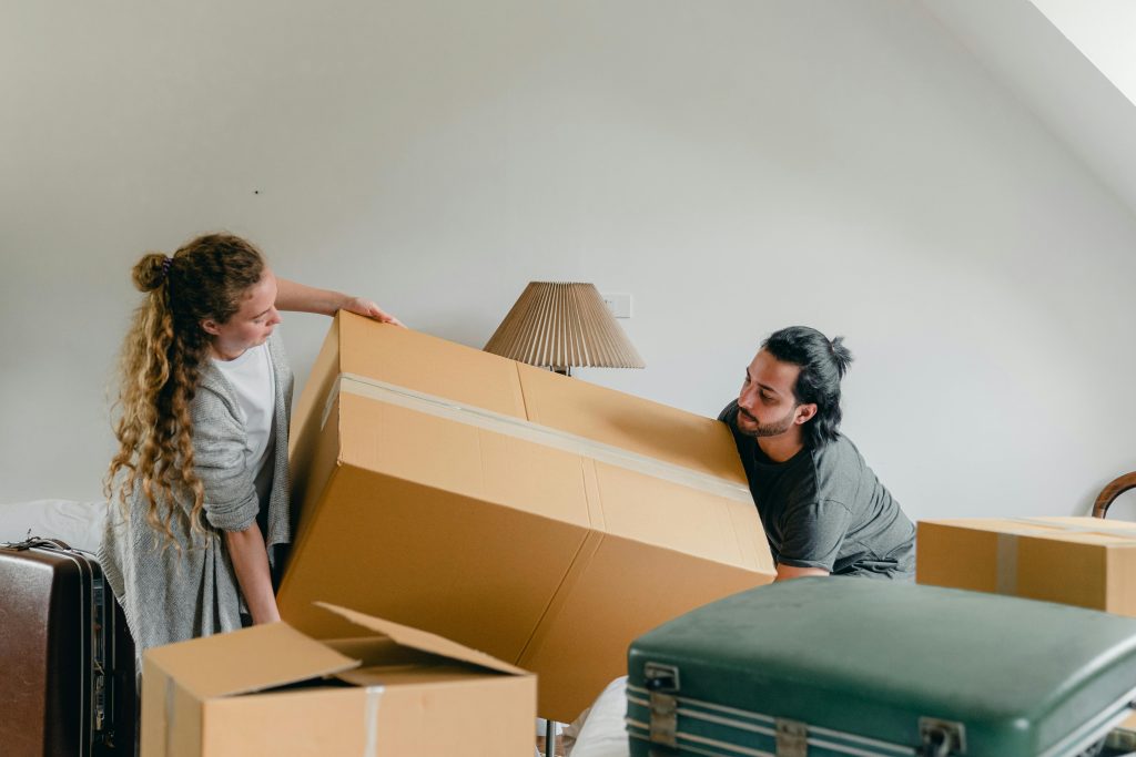 A couple moves a large cardboard box in their new apartment during a relocation.